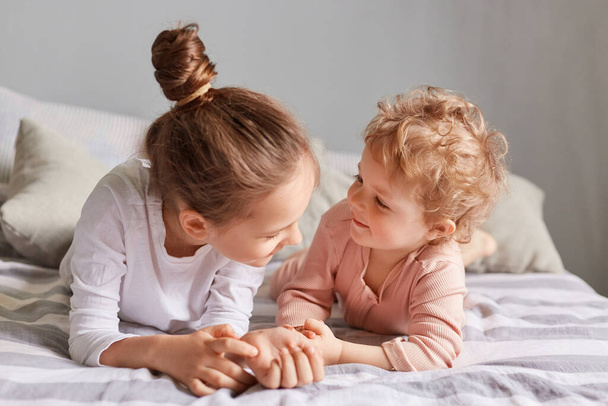 Playful children. Happy childhood. Lazy morning. Cute little girls playing in bedroom lying in bed siblings spending time together. - Fotografie, Obrázek
