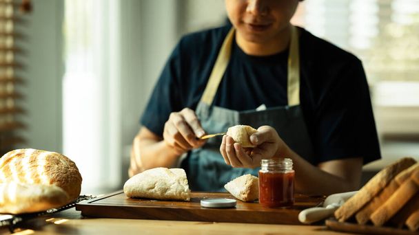 Man verspreidt zoete frambozenjam op brood tijdens het ontbijt of brunch in de keuken. - Foto, afbeelding