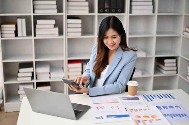 Professional millennial Asian businesswoman or female financial analyst working on business financial data, preparing financial report, working at her desk in the office. - 写真・画像