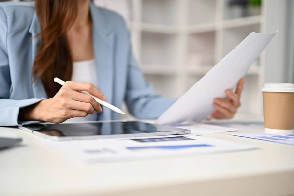 Imagen de cerca de una mujer de negocios que usa su tableta digital mientras revisa el informe de negocios en su escritorio. - Foto, imagen