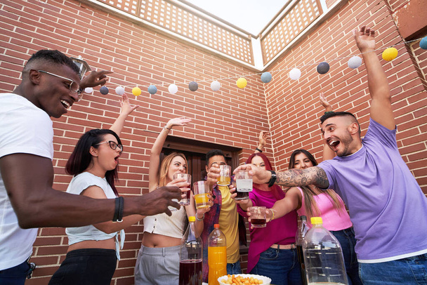 Group of happy friends toasting with drinks while enjoying an outdoor party on a terrace. Friendship concept. - Photo, image