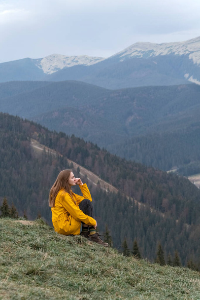 La chica se sienta a un lado de la montaña. Mujer joven en las montañas disfrutando de aire limpio. Vista vertical - Foto, imagen