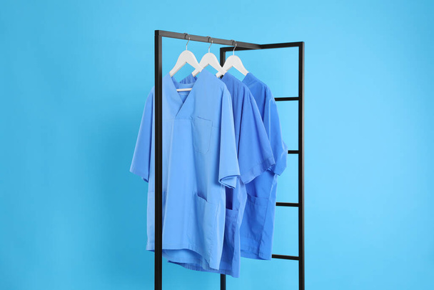 Medical uniforms on metal rack against light blue background - Foto, imagen