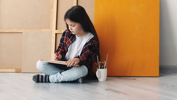 Painting time. Kids creativity. Inspired hobby. Little girl sitting floor drawing on paper in light room interior. - Foto, Imagen