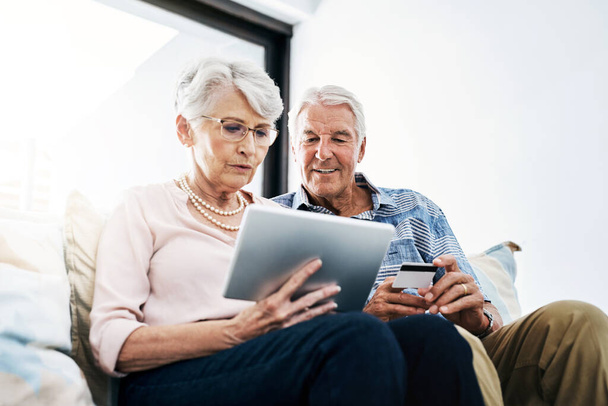 Mantenerse al día con los pagos de la manera conveniente. una pareja mayor haciendo un pago con tarjeta de crédito en una tableta digital en casa - Foto, Imagen