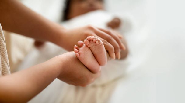 Young african american female hold cute legs of little child, lie on bed, rest in children room, cropped, blurred. Family, kid care, motherhood and love, mom and baby at home - Φωτογραφία, εικόνα