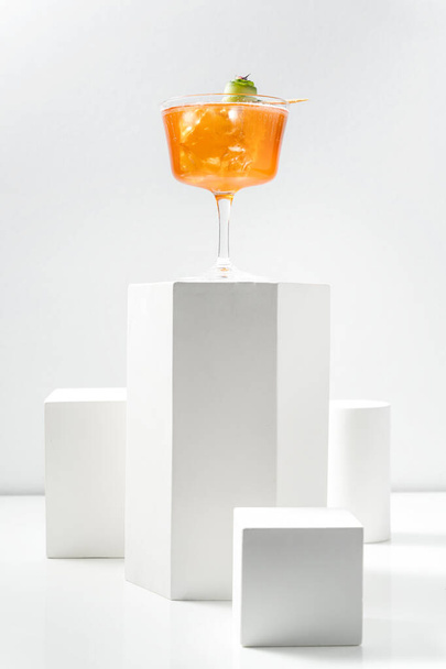 Aperol Spritz cocktail met ijsblokjes en een plakje komkommer in een transparant steelglas. De cocktail staat op een gipsen figuur tussen andere gipsen figuren op een witte achtergrond. - Foto, afbeelding