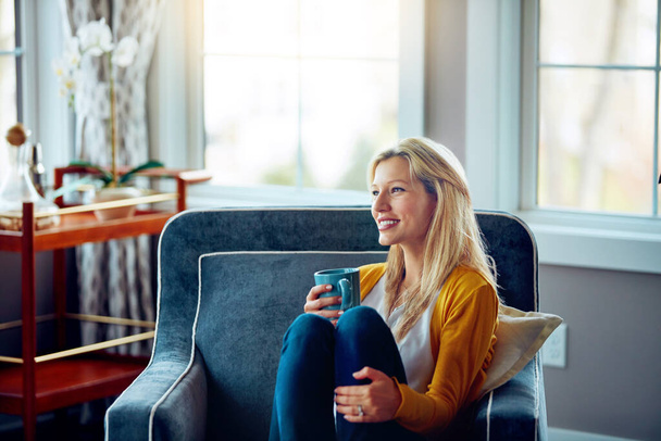 Toma tiempo para reflexionar. una joven relajándose en su sofá con una taza de café - Foto, Imagen