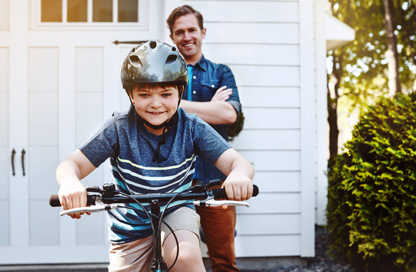 Le lezioni di ciclismo da papà hanno finalmente dato i loro frutti. un ragazzo in bicicletta con il padre sullo sfondo - Foto, immagini