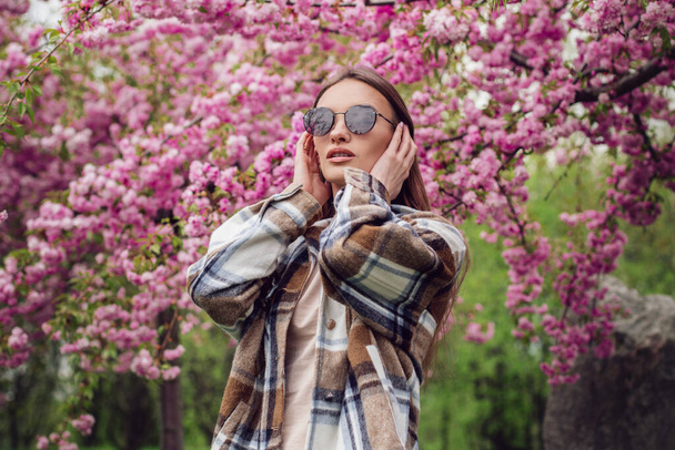 portrait of charming fashionable woman in blooming sakura park - Фото, зображення