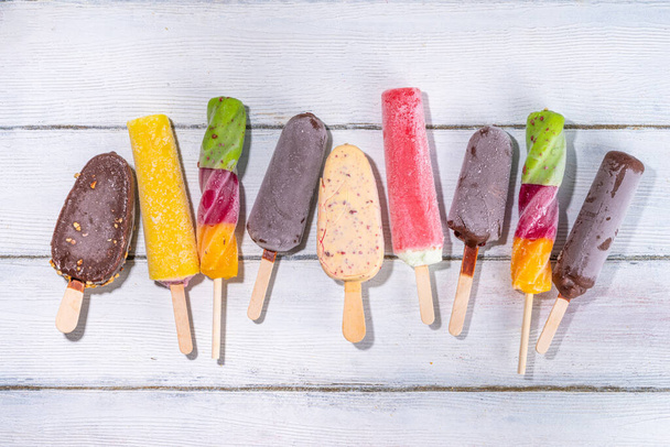 Various ice cream popsicle on white wooden background, summer sweets, dessert, vacation and holiday background, Set of assorted flavors popsicle lollipops - chocolate, vanilla, fruit, rainbow  - Fotografie, Obrázek