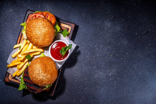 Healthy veggie burgers with vegetable cutlets. Homemade beetroot and carrot burgers, with fresh vegetables, vegan mayo tomato sauce, whole grain buns, on dark background with ingredients, copy space - Foto, Imagem