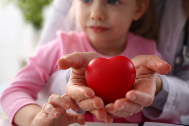 Hands of child and cardiologist doctor with red heart closeup. Treatment of heart disease in children - Foto, immagini