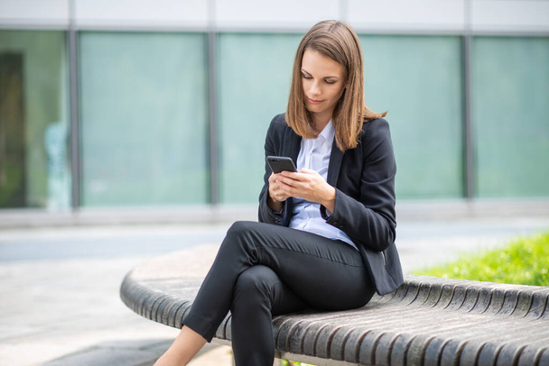 Portrait of a young woman using phone sitting on a bench outdoor - Foto, immagini