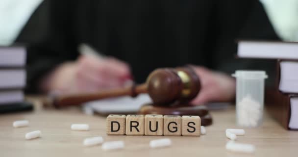Белые таблетки и словесные наркотики на деревянных кубиках рядом с судьей молотком крупным планом 4К кино замедленной съемки. Уголовная ответственность за приобретение и хранение наркотиков - Кадры, видео