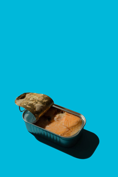 Open tin can with salmon on a blue background with hard shadows, the concept of red canned fish on the sea or in the ocean - Fotoğraf, Görsel