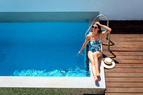 Полная длина привлекательной женщины в купальниках и солнцезащитных очках во время отдыха в бассейне. Выстрел сверху. - Фото, изображение