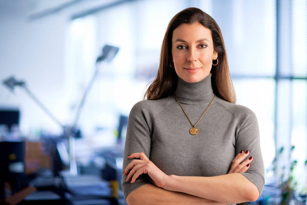 Shot of a mid aged businesswoman looking at camera while standing at the office. Brunette haired female wearing turtleneck sweater and smiling. Copy space.  - 写真・画像