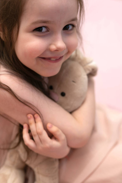 Una chica, una morena de siete años con una liebre de felpa en sus manos. Foto de alta calidad - Foto, Imagen