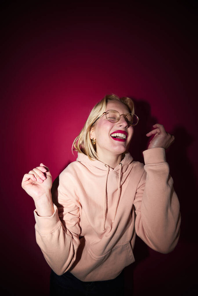 Une jeune femme blonde joyeuse dansant dans un studio isolé sur fond de magenta. Viva magenta, couleur de l'année. - Photo, image