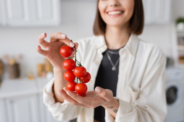 Vista recortada de mujer sonriente borrosa sosteniendo tomates cherry en la cocina  - Foto, imagen