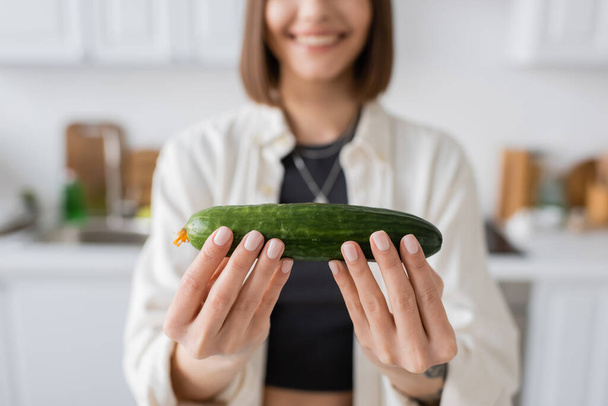 Cropped view of blurred woman holding ripe cucumber in kitchen  - Фото, зображення