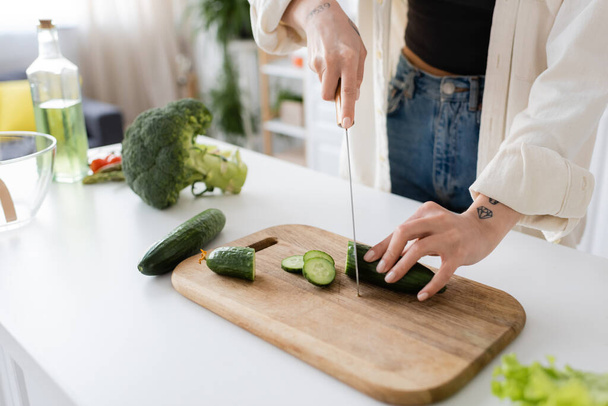 Cropped view of young woman cutting fresh cucumber in kitchen  - Photo, Image