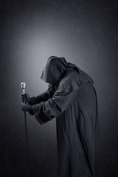 Wizard with hooded cape and magic staff over dark misty background - Foto, afbeelding
