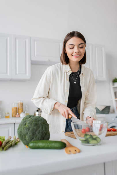 Smiling young woman cutting vegetables while cooking salad in kitchen  - Foto, Imagem
