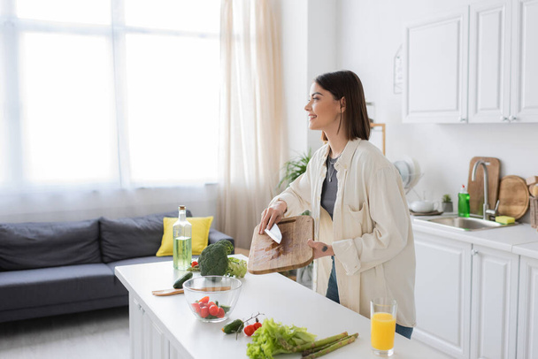 Widok z boku uśmiechnięta kobieta gotowanie świeżej sałatki w kuchni  - Zdjęcie, obraz