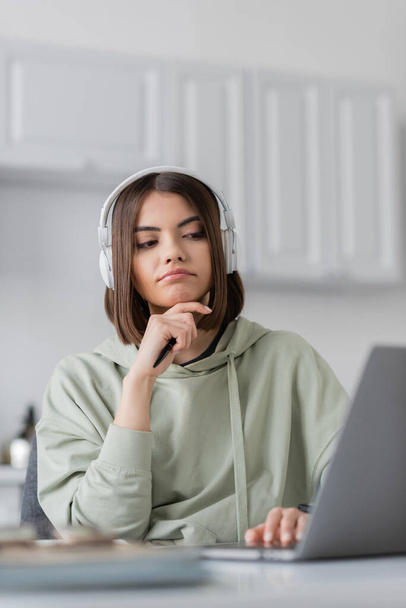 Pensive freelancer in headphones using blurred laptop at home  - Foto, Imagem