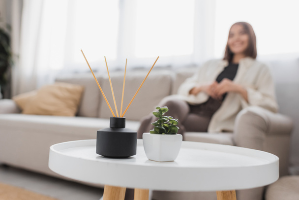 Bamboo aroma sticks and plant on coffee table near blurred woman at home  - Foto, immagini