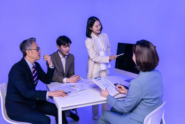 Asian Korean senior, middle aged and young male and female colleagues models in business attire, neon purple studio background, present with confidence concept - Zdjęcie, obraz