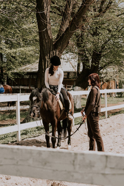 A woman instructor teaching girl how to ride a horse.  Female rider practicing on a horseback learning equestrian sport. Active lifestyle and leisure activity concept - Photo, Image