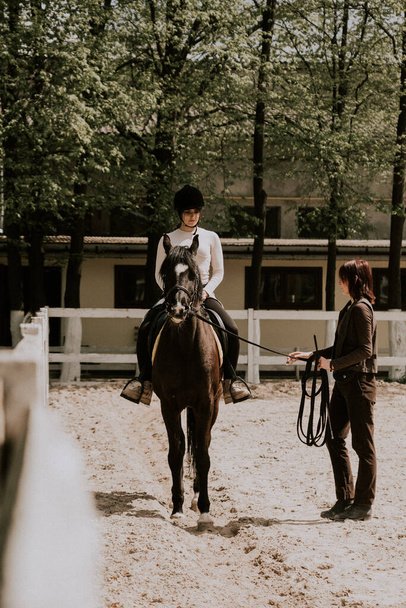 A woman instructor teaching girl how to ride a horse.  Female rider practicing on a horseback learning equestrian sport. Active lifestyle and leisure activity concept - Φωτογραφία, εικόνα