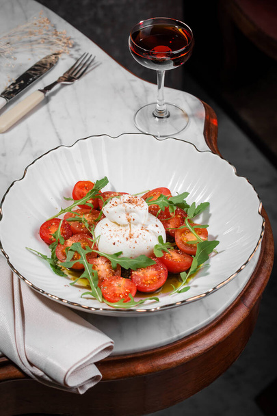 Queso burrata en un plato blanco con tomates y ensalada de rúcula con aceite de oliva comida italiana tradicional. - Foto, imagen