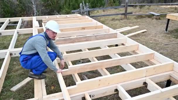 Muž, který staví dřevěný rámový dům na pilotní základně. Tesař měří dřevěná prkna. Koncept tesařství. - Záběry, video
