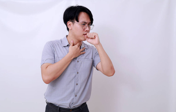 アジア人男性は喉を守りながら咳をする。白地に隔離された - 写真・画像