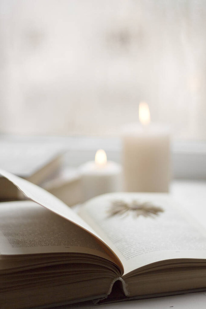 Old books and candles. Cozy postcard. White flowers. Romantic photo. A simple winter decoration on the windowsill. - Zdjęcie, obraz