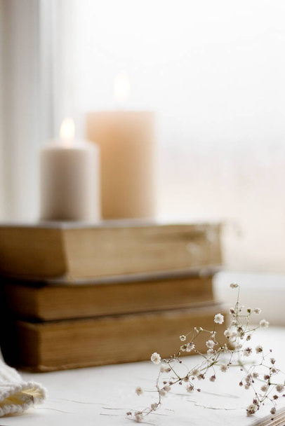 Old books and candles. Cozy postcard. White flowers. Romantic photo. A simple winter decoration on the windowsill. - Photo, image