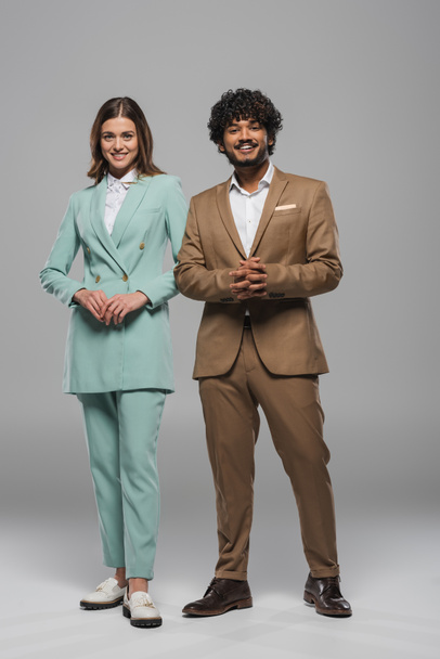 Full length of cheerful interracial event hosts in formal wear standing together and looking at camera during party on grey background  - Zdjęcie, obraz
