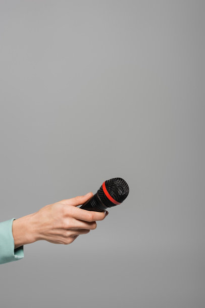 Oříznutý pohled na černý bezdrátový mikrofon v ruce s hostitelem akce v zelené bundě během vystoupení na dovolené při stání izolovaný na šedé   - Fotografie, Obrázek
