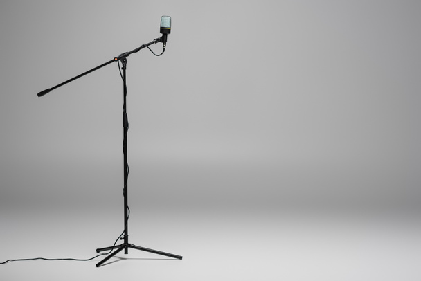 Black microphone with wire on metal stand on grey background with copy space  - Fotó, kép