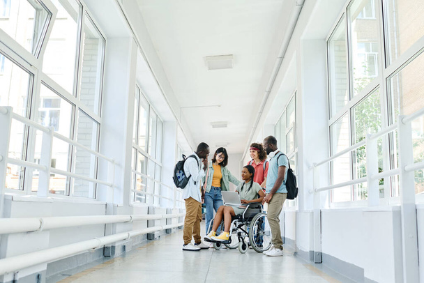 Gruppo di studenti che utilizzano il computer portatile insieme durante la pausa mentre in piedi nel corridoio della scuola - Foto, immagini