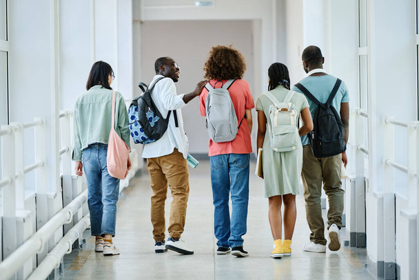 Achteraanzicht van een groep leerlingen met rugzakken die na de lessen door de schoolgang lopen - Foto, afbeelding