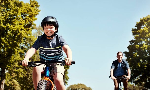 Давай, пап, не отставай. a young boy and his father riding together on their bicycle - Фото, изображение