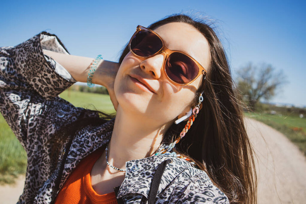 Porträt der jungen glücklichen brünetten Frau lächelnd Porträt aus nächster Nähe. Junge Frau auf Reisen. Stilvoll gekleidetes Hipstermädchen mit Sonnenbrille in Leopardenjacke an einem sonnigen Tag. Selfie-Foto für Frauen.  - Foto, Bild