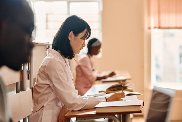 Asiatico studente di medicina in camice bianco prova di scrittura a scrivania durante la lezione presso l'università - Foto, immagini