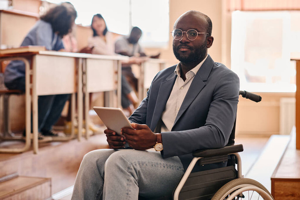 Portret van een Afrikaanse leraar met een handicap die op een rolstoel zit met behulp van een digitale tablet tijdens een lezing aan de universiteit - Foto, afbeelding