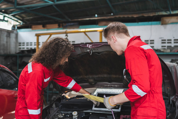 Young Caucasian car mechanic with a checklist, Mechanics in uniform are working in auto service, Technician checking modern car at garage, Car repair and maintenance concepts - Fotó, kép